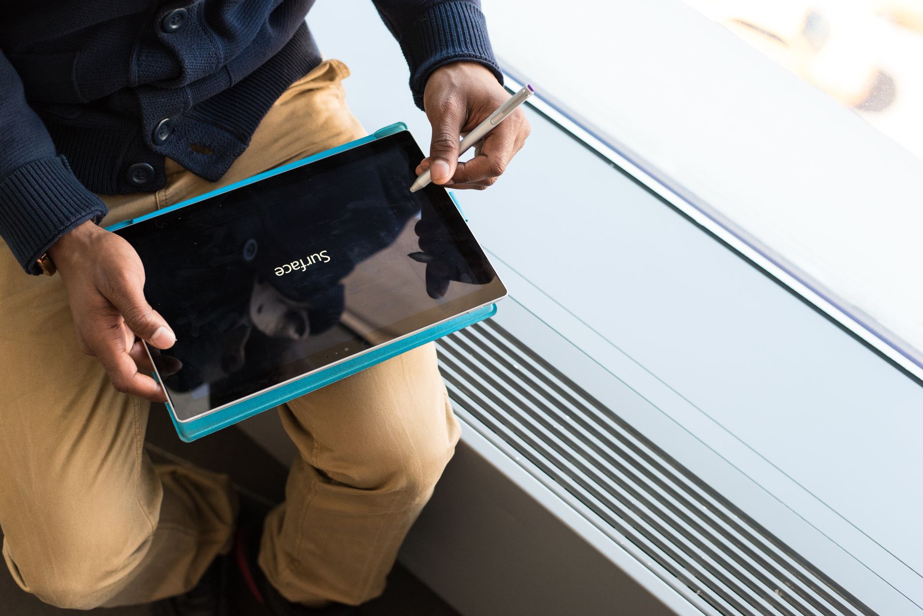 A person holds a stylus over a tablet resting on their lap