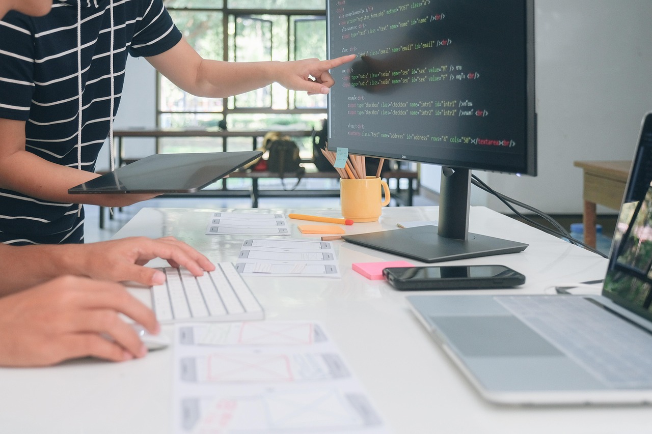 Two developers collaborate on web application code, pointing at the monitor display
