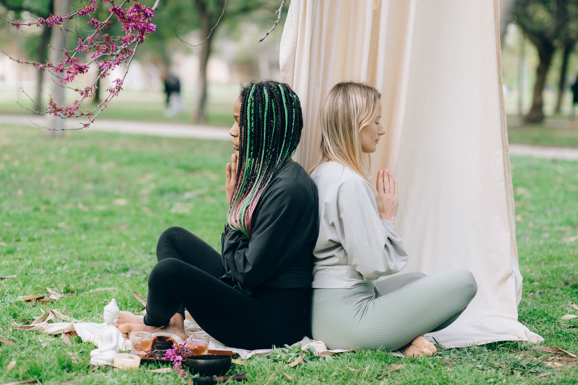 Two diverse women meditate back-to-back outdoors, finding inner peace at a retreat