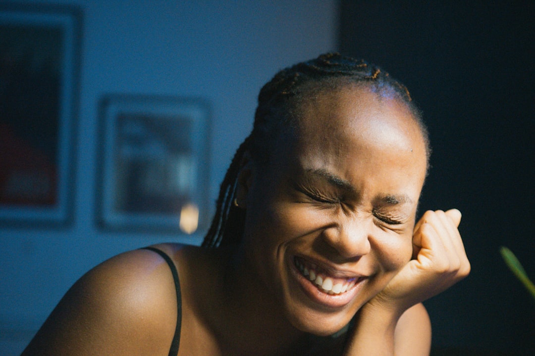 A Black woman in braids laughs heartily with eyes closed, hand on her chin