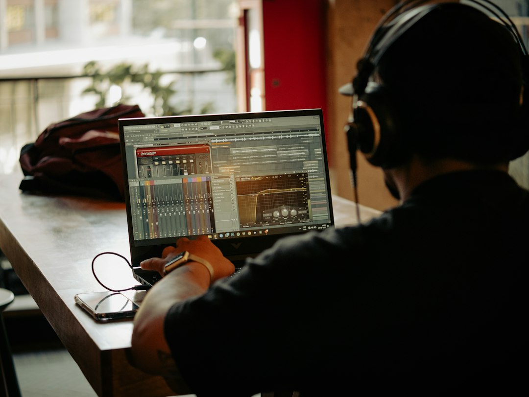A person wearing headphones works with audio editing software on a laptop