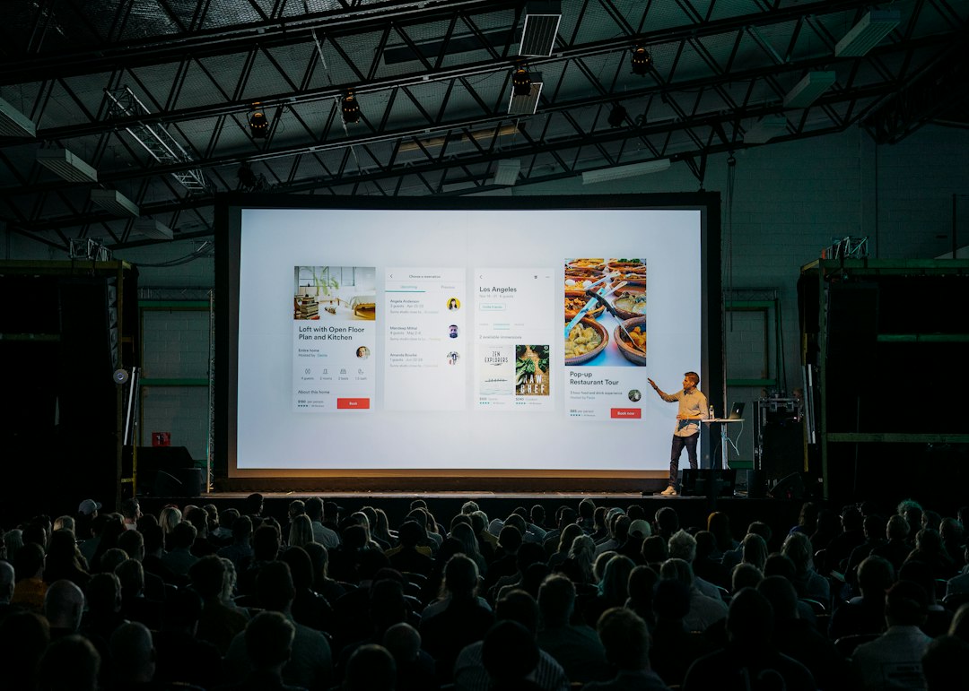 A speaker presents mobile app slides on a screen to a seated audience
