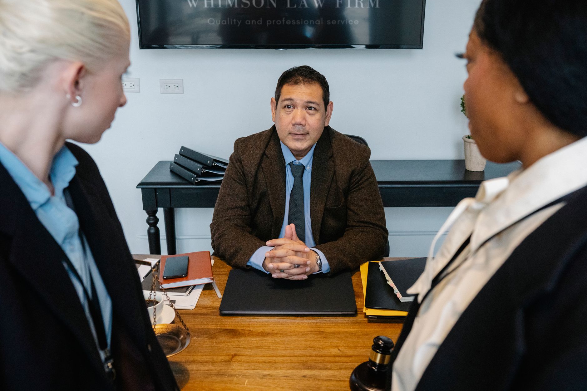 A male lawyer advises two female clients at a law firm desk