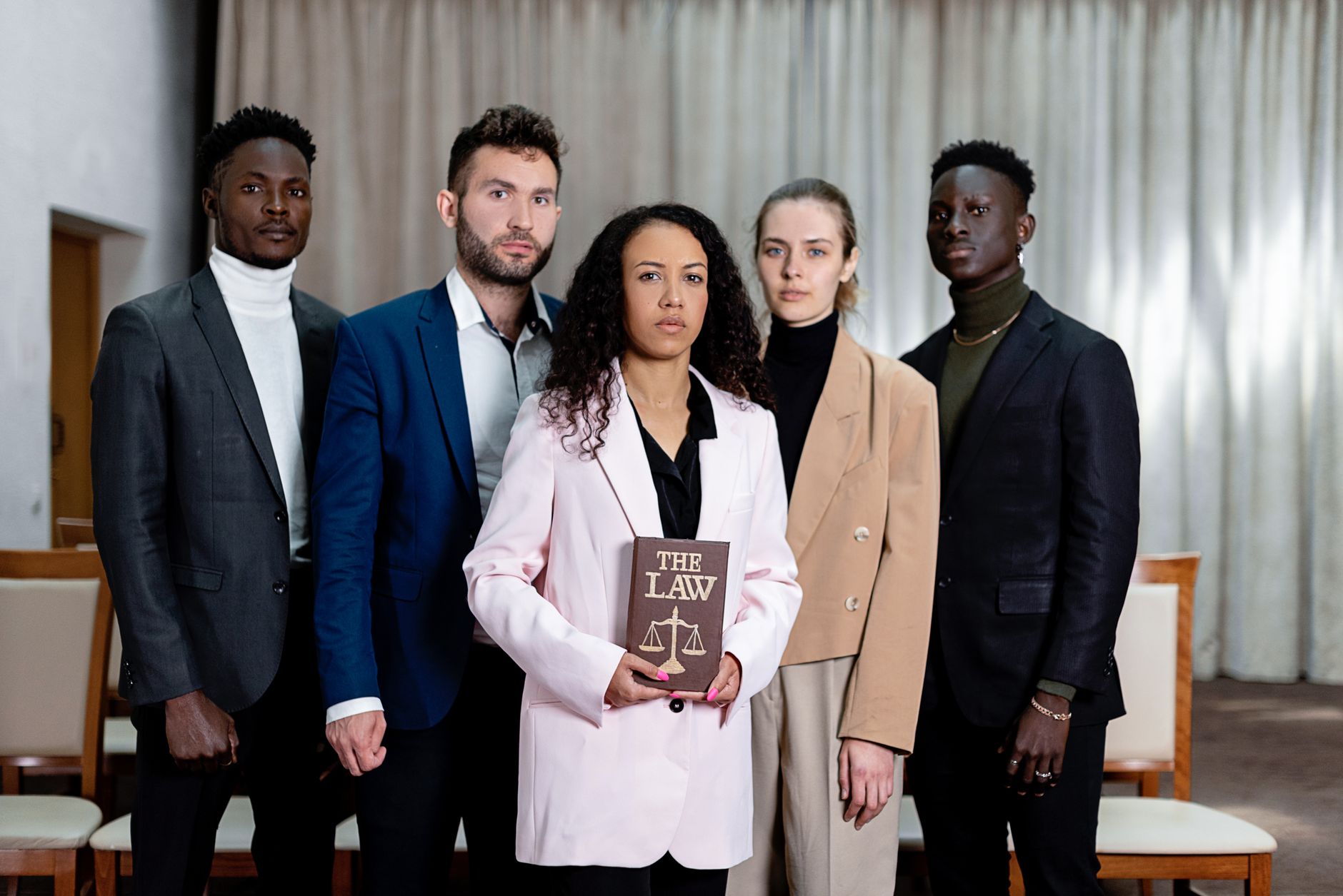 Diverse group of corporate legal advisors standing together, one holding "The Law" book