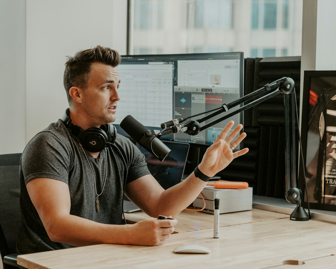Man with headphones and microphone speaking, gesturing at a podcasting setup