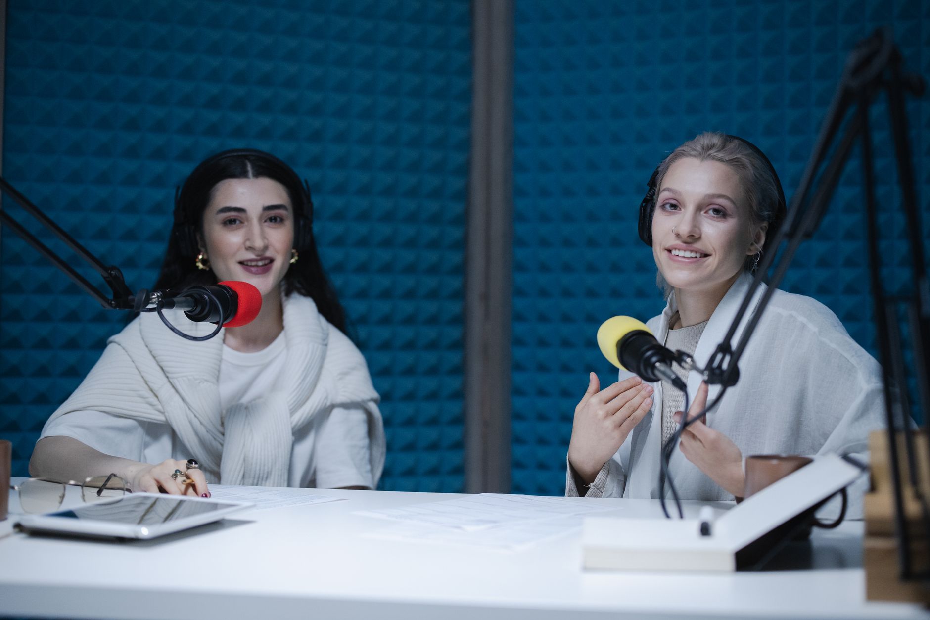 Two smiling women recording a podcast with microphones in a sound studio