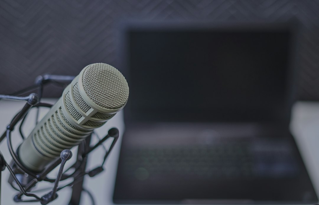 A gray podcast microphone on a stand with a blurred laptop in the background