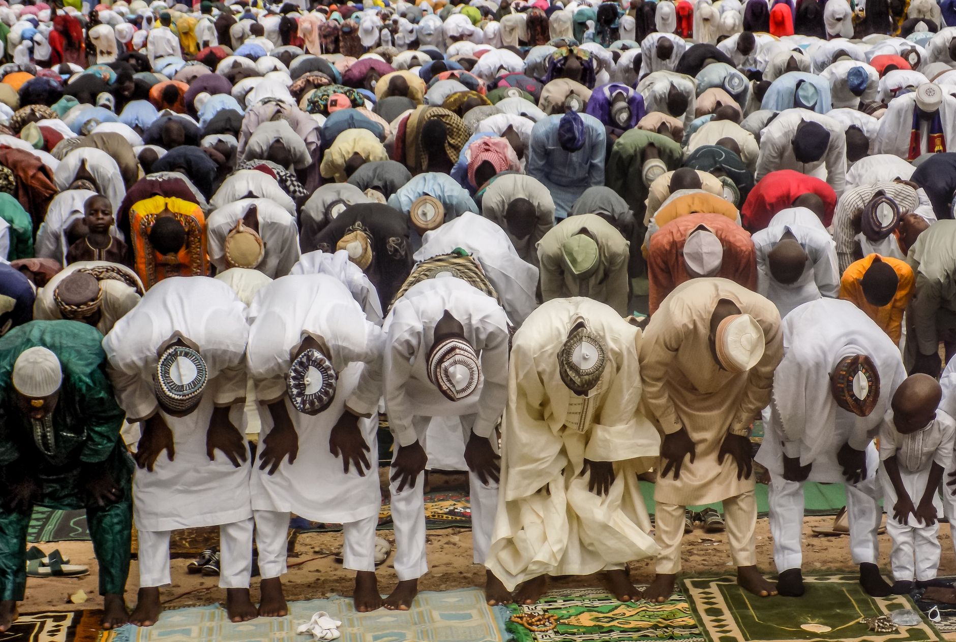 Many men and boys perform a large religious bowing prayer on mats outdoors