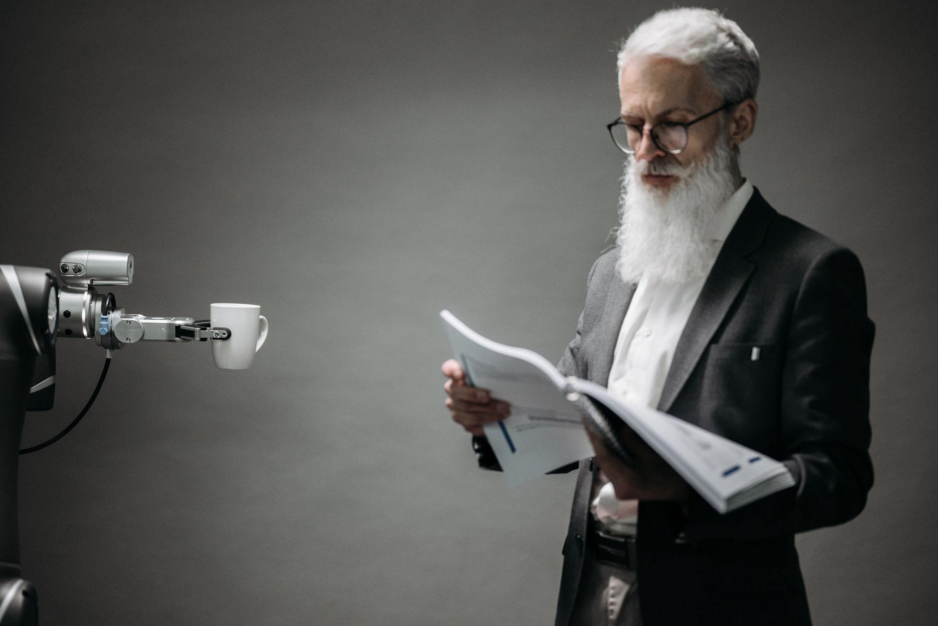 A robot arm holds a coffee cup near a man reading documents