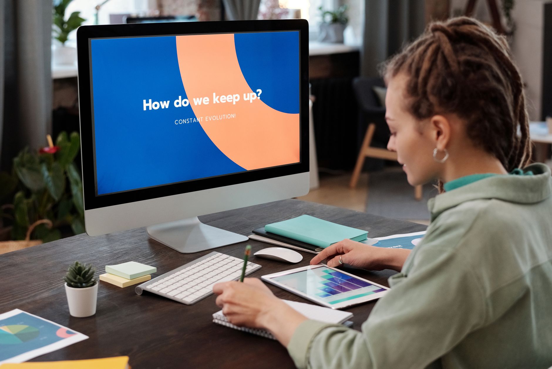 A woman takes notes at a desk in front of a computer monitor