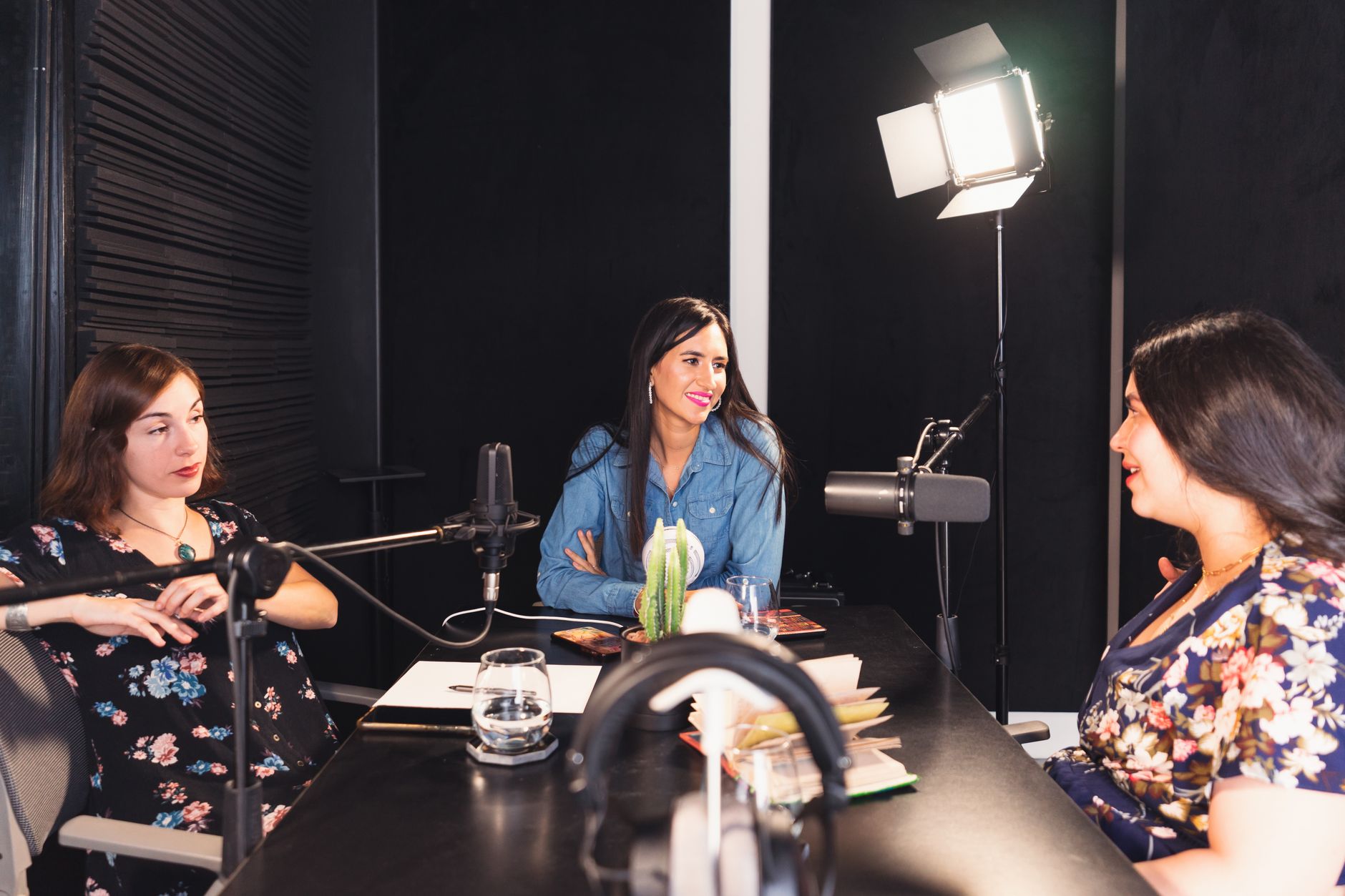 Three women discussing in a professional podcast recording studio with microphones