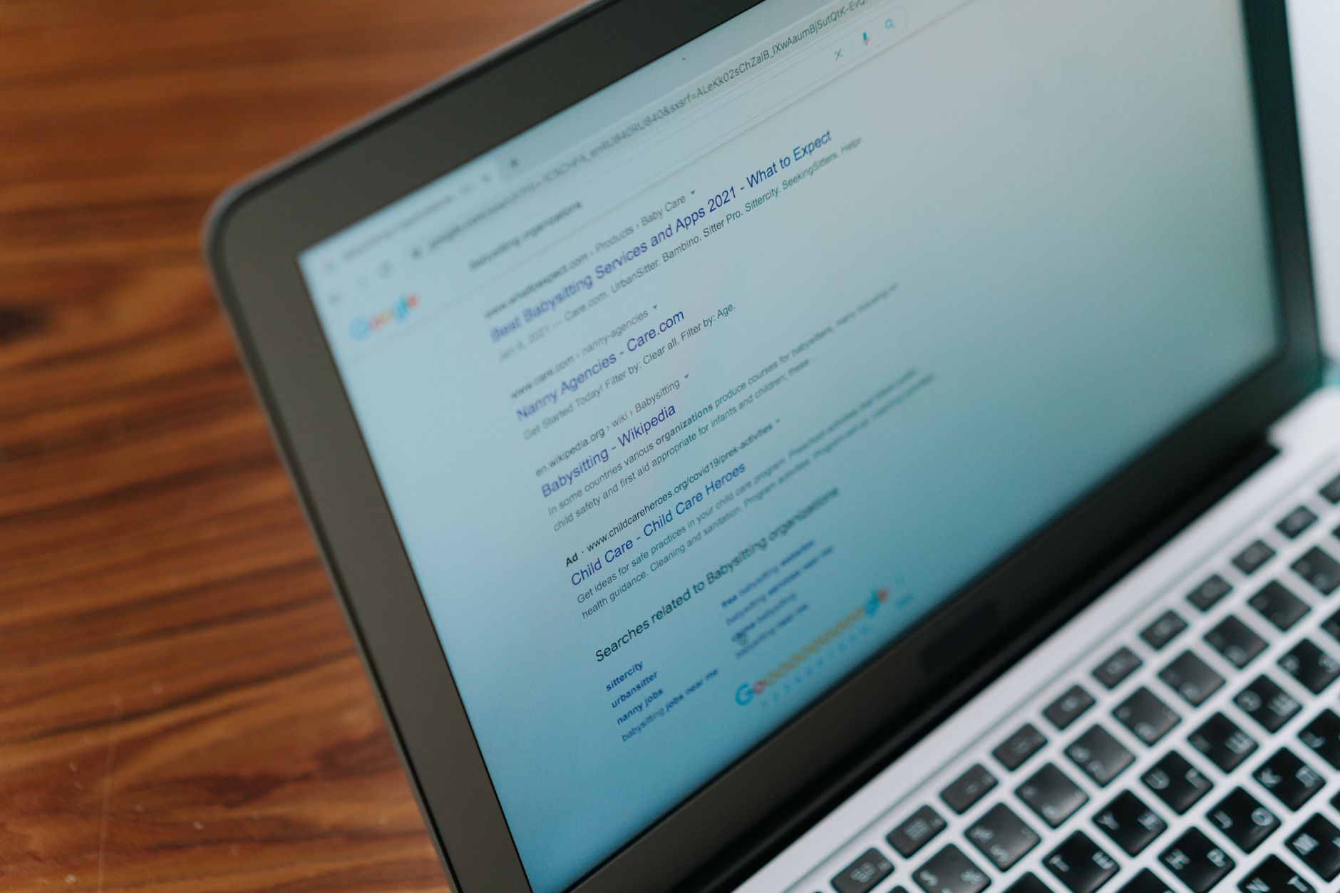 Laptop screen displays Google search results for babysitting and child care agencies