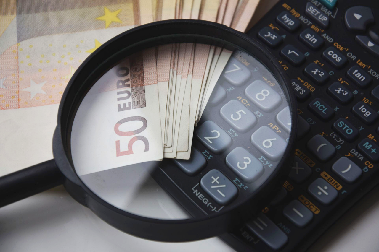 Magnifying glass on Euro banknotes and a calculator, representing website cost analysis