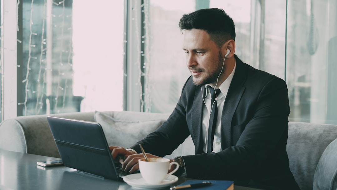 Man in a suit wearing earbuds works on a laptop with coffee, representing hidden costs
