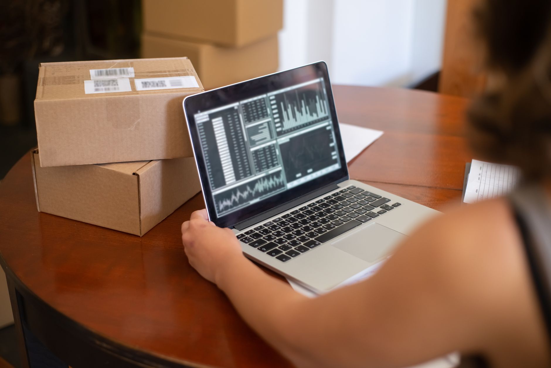 Person analyzing data on a laptop, with two shipping boxes nearby on a wooden desk