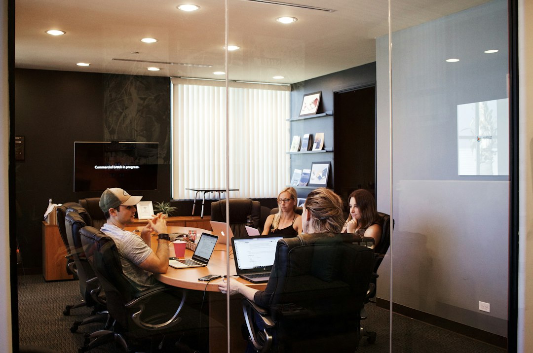 Four people sit around a wooden conference table with open laptops