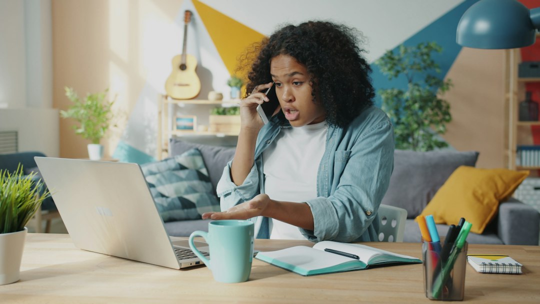 A woman gestures at an open laptop while talking on a mobile phone