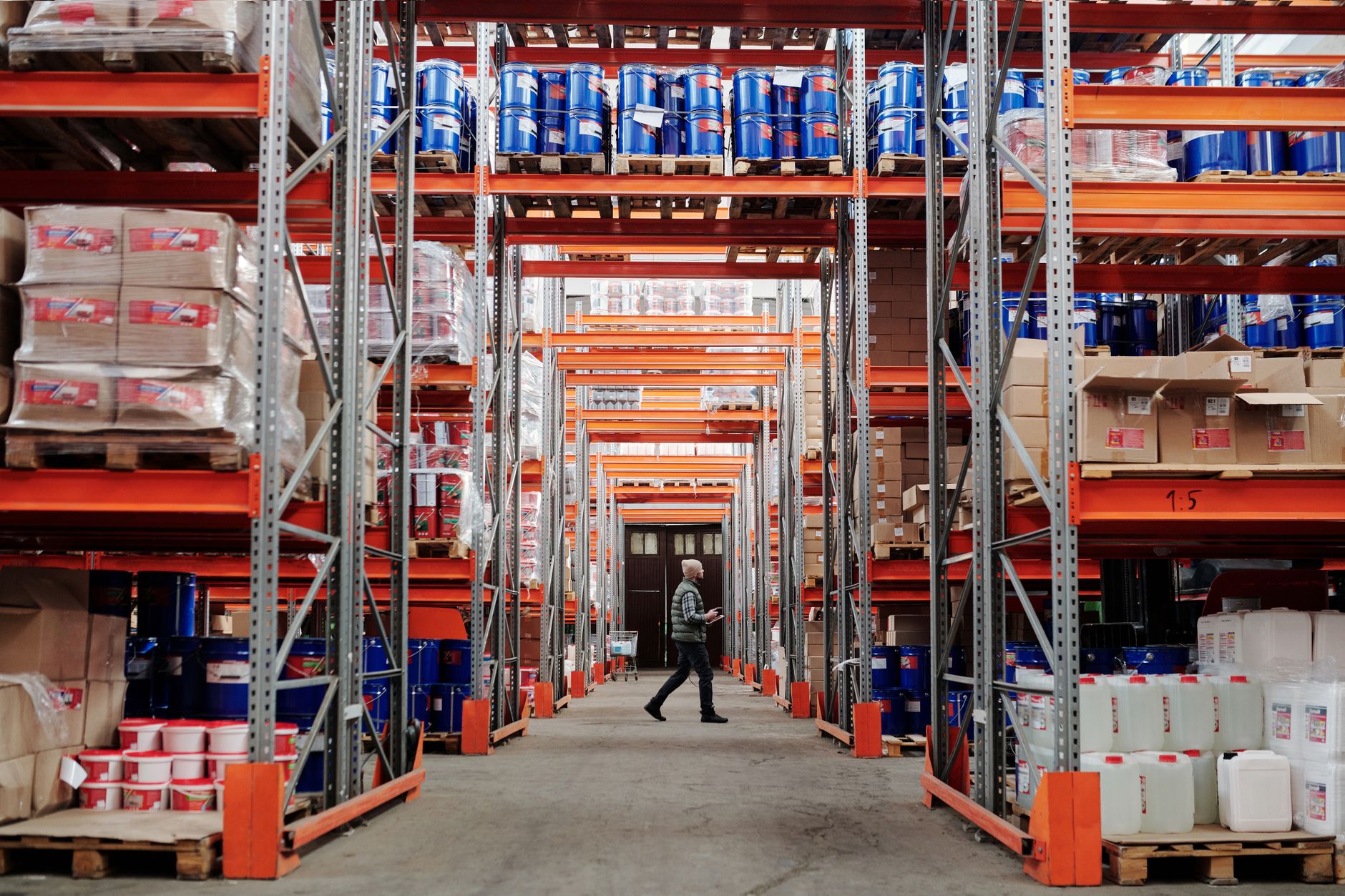 A person walks down a warehouse aisle lined with tall racks of goods