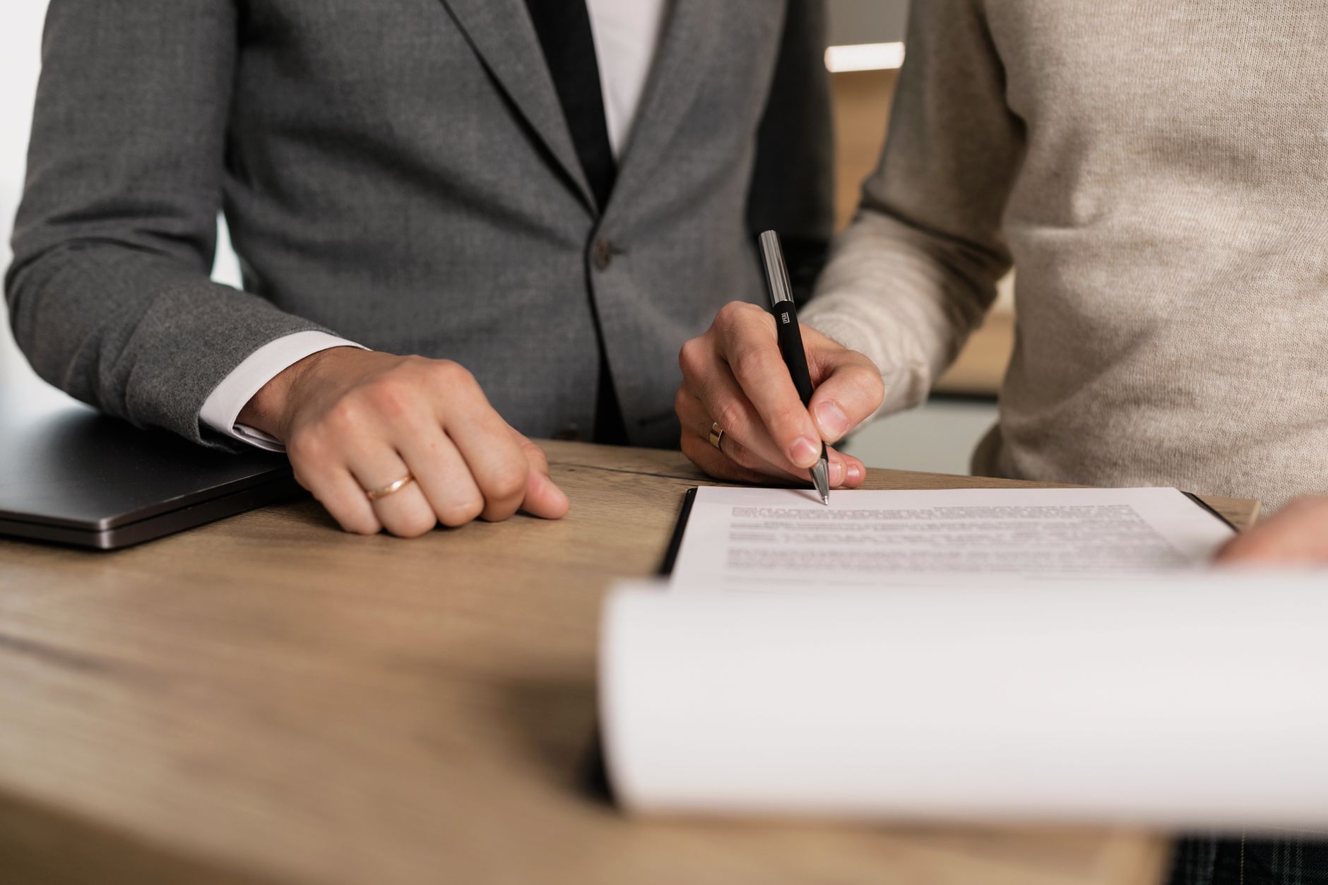 A person in a suit signing a document while another looks on