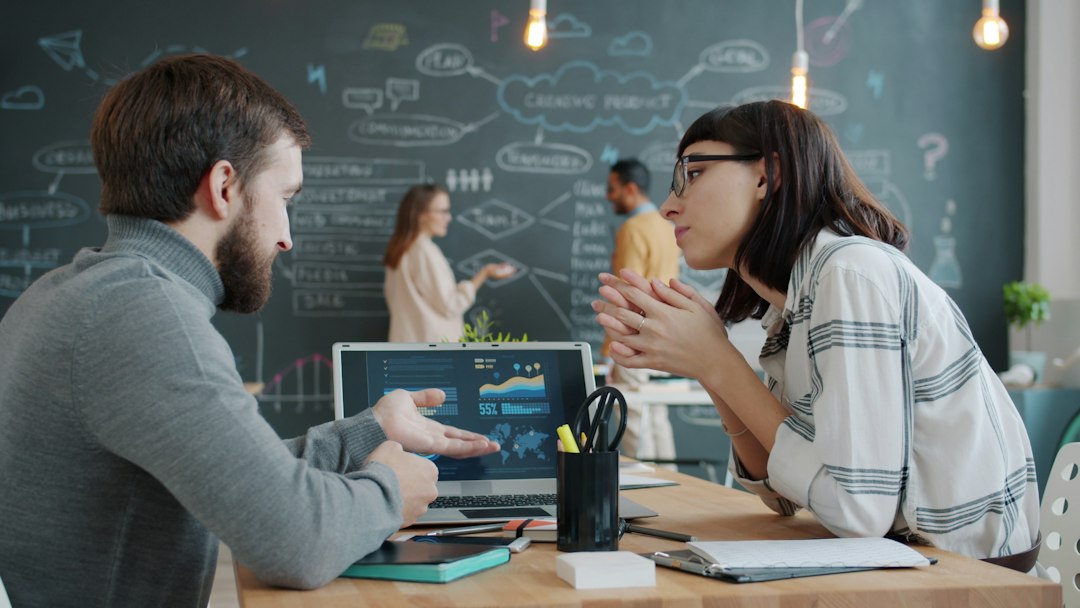 Two business professionals discussing data on a laptop with charts and graphs