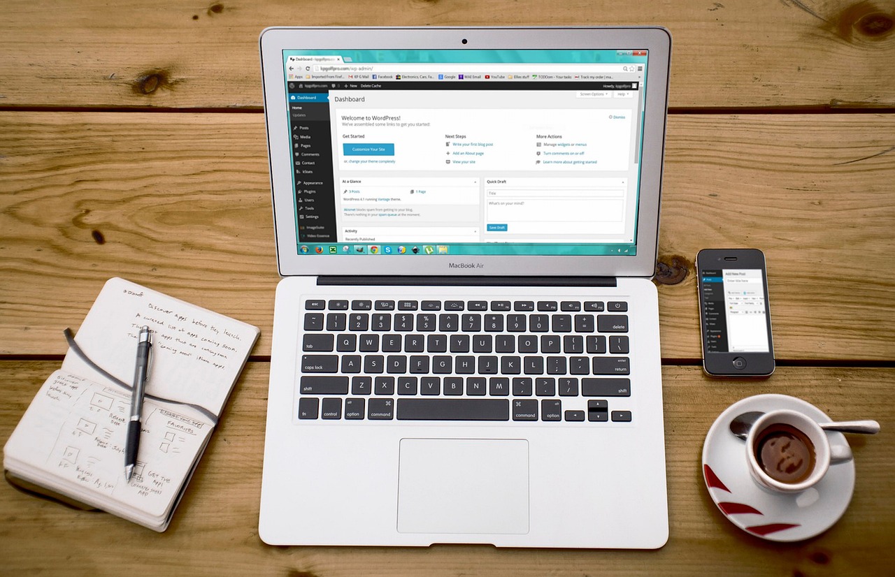 Laptop open to WordPress dashboard on a wooden desk with coffee and notebook