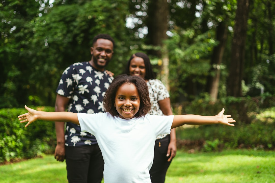 Smiling young Black girl with arms out, parents smiling behind her in a park