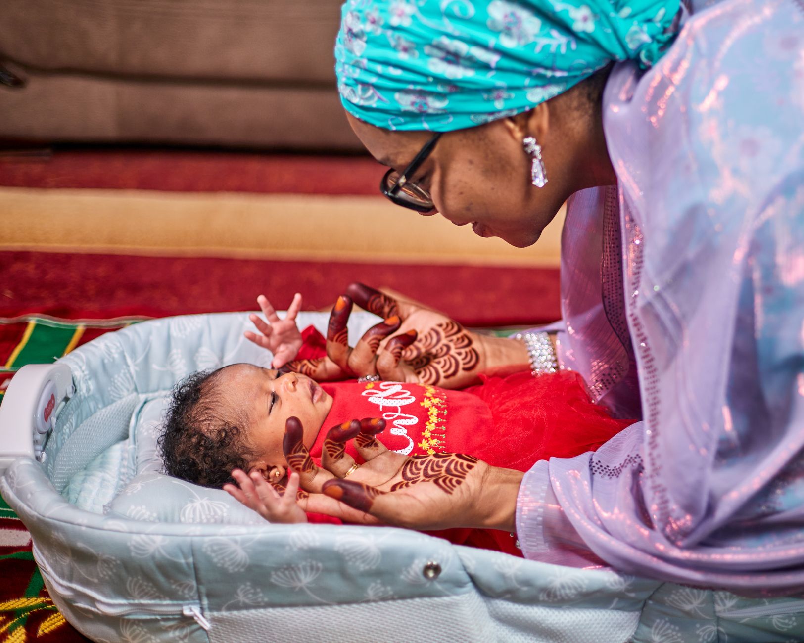 Woman with henna hands gently looks at a newborn baby in a bassinet
