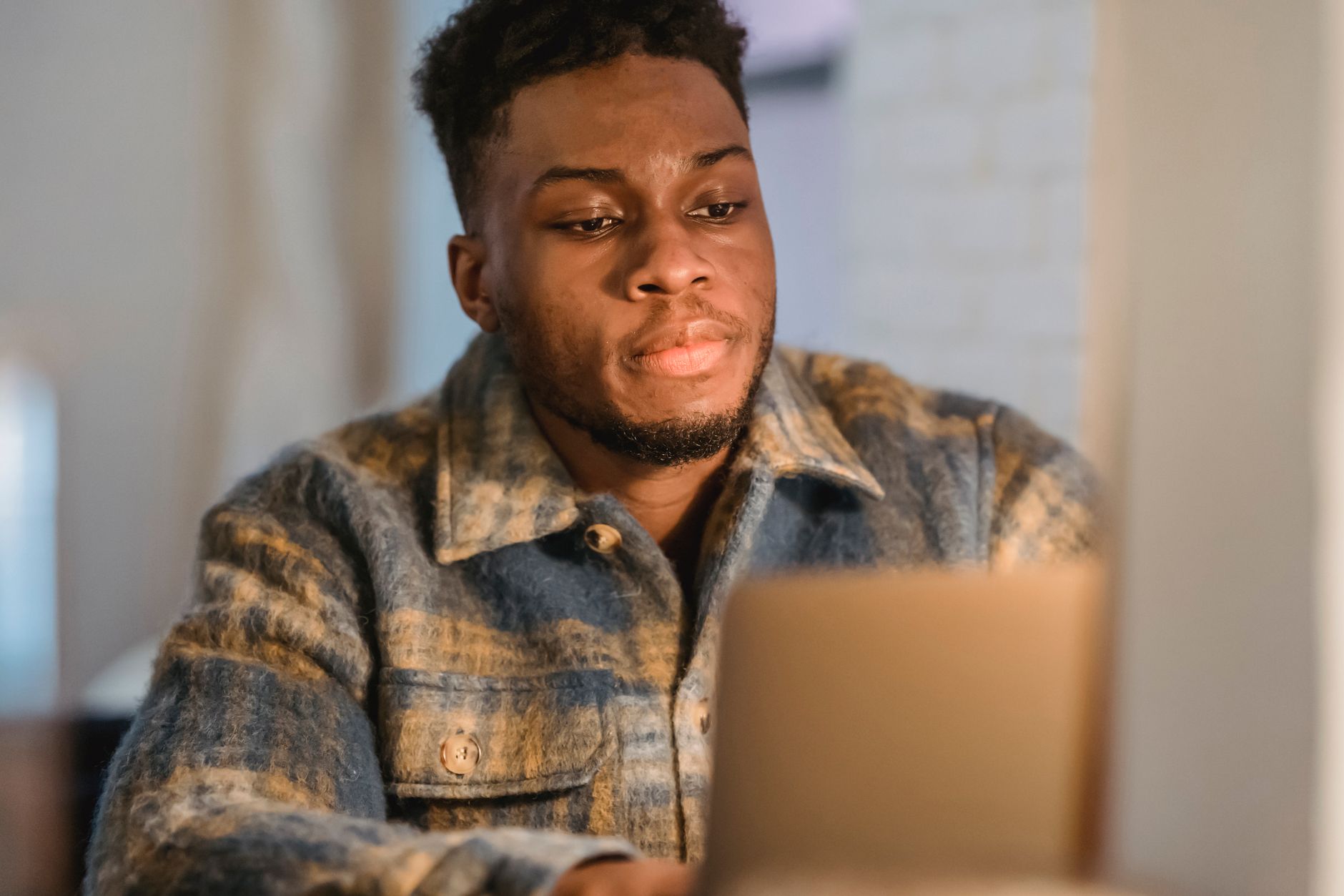 A young man in a plaid jacket looks at a laptop screen