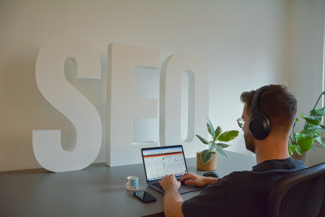 A man wearing headphones types on a laptop beside large white SEO letters