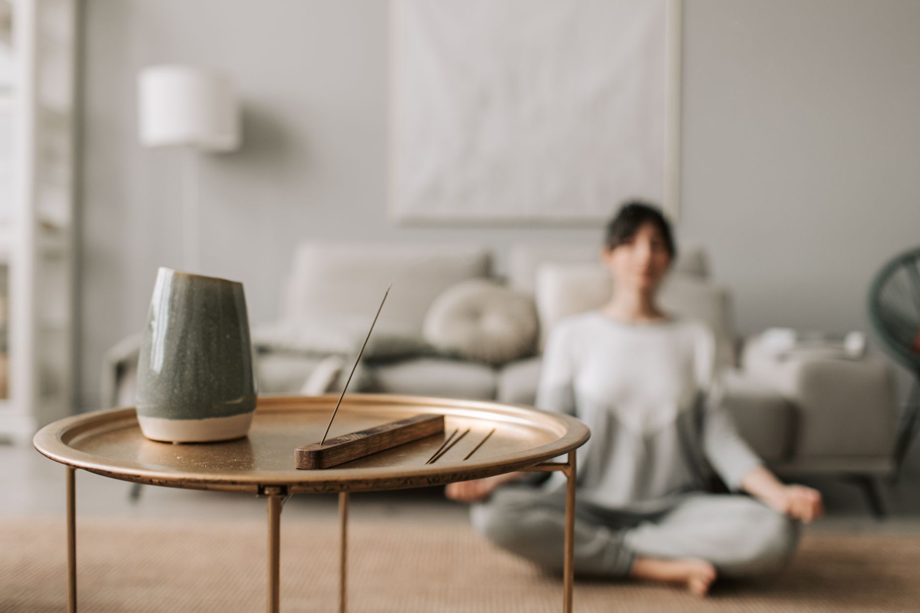A blurred person meditates in the background behind a table with incense