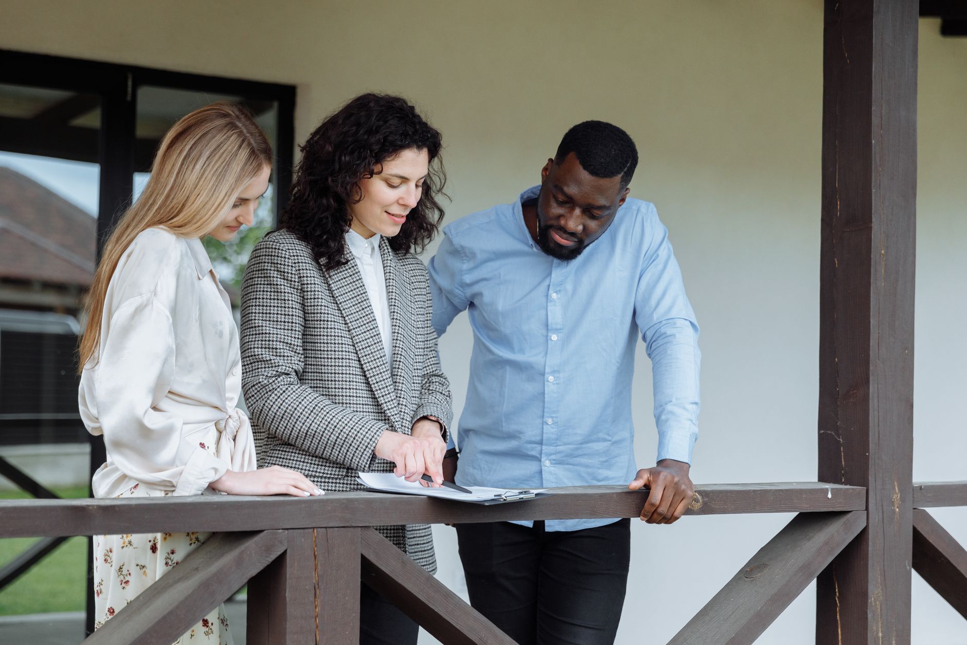 Three people review property valuation documents on a porch balcony