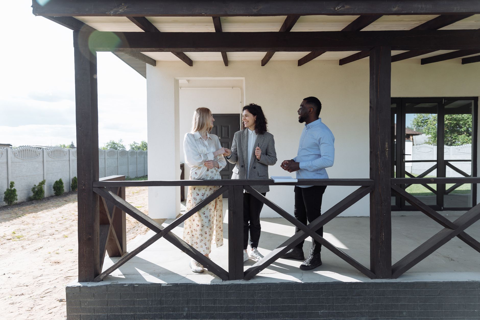 Three people discussing property on a porch, likely with a real estate agent