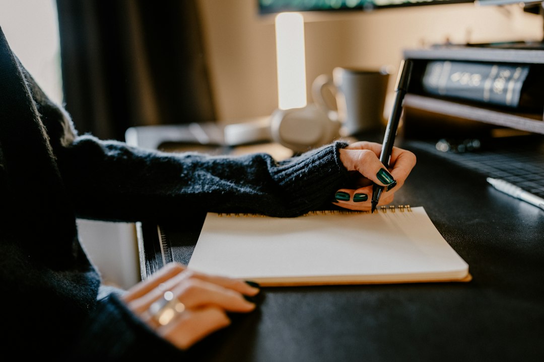 A person writes with a black pen in a blank spiral notebook