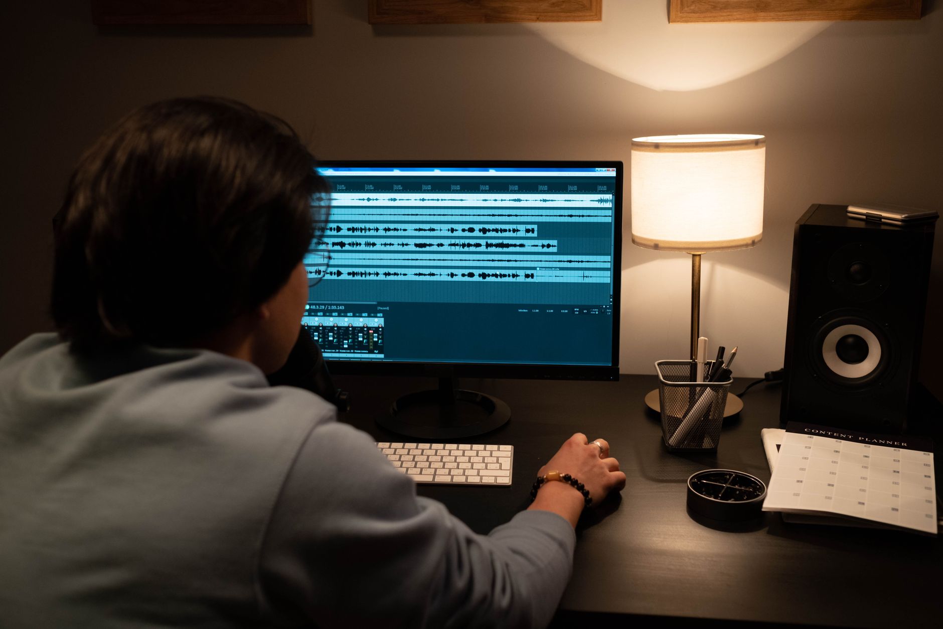 A person sits at a desk viewing audio waveforms on a computer monitor