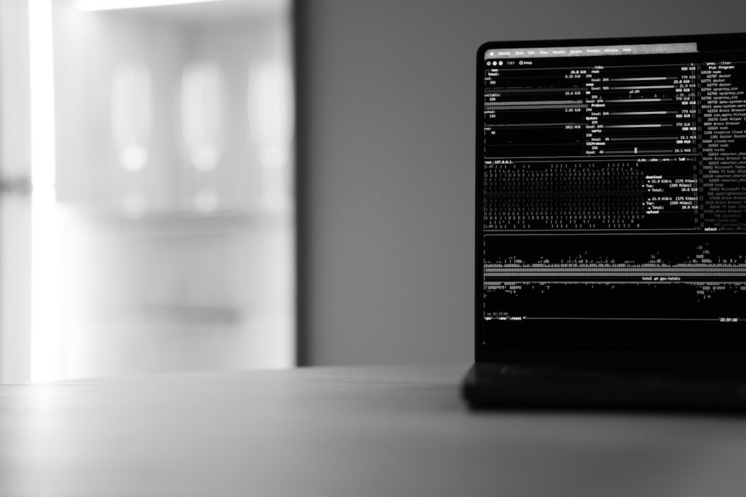 A laptop on a desk displays computer terminal text on a dark screen