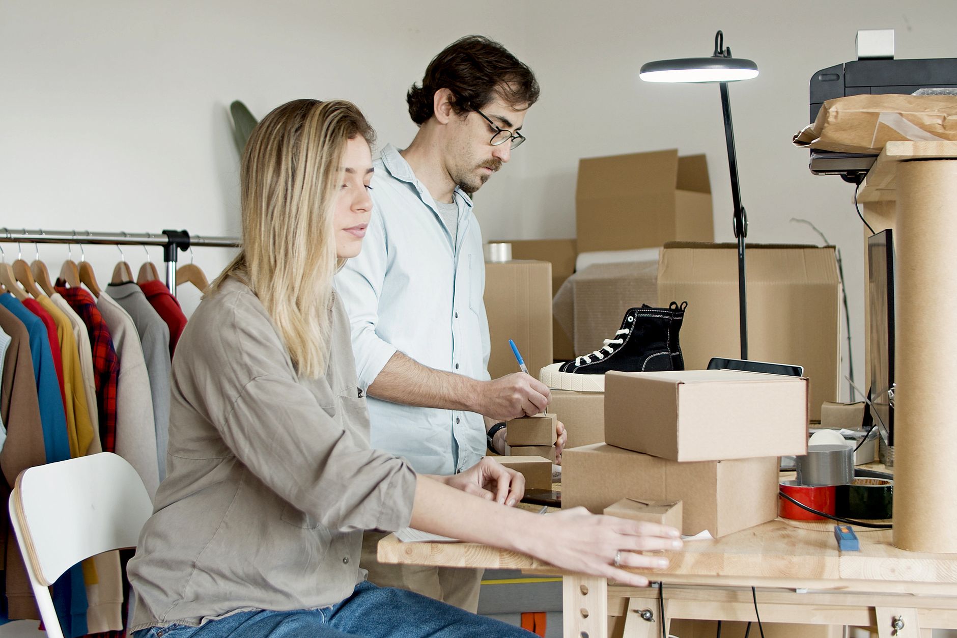 Two people preparing e-commerce orders with packages and clothes in a small space