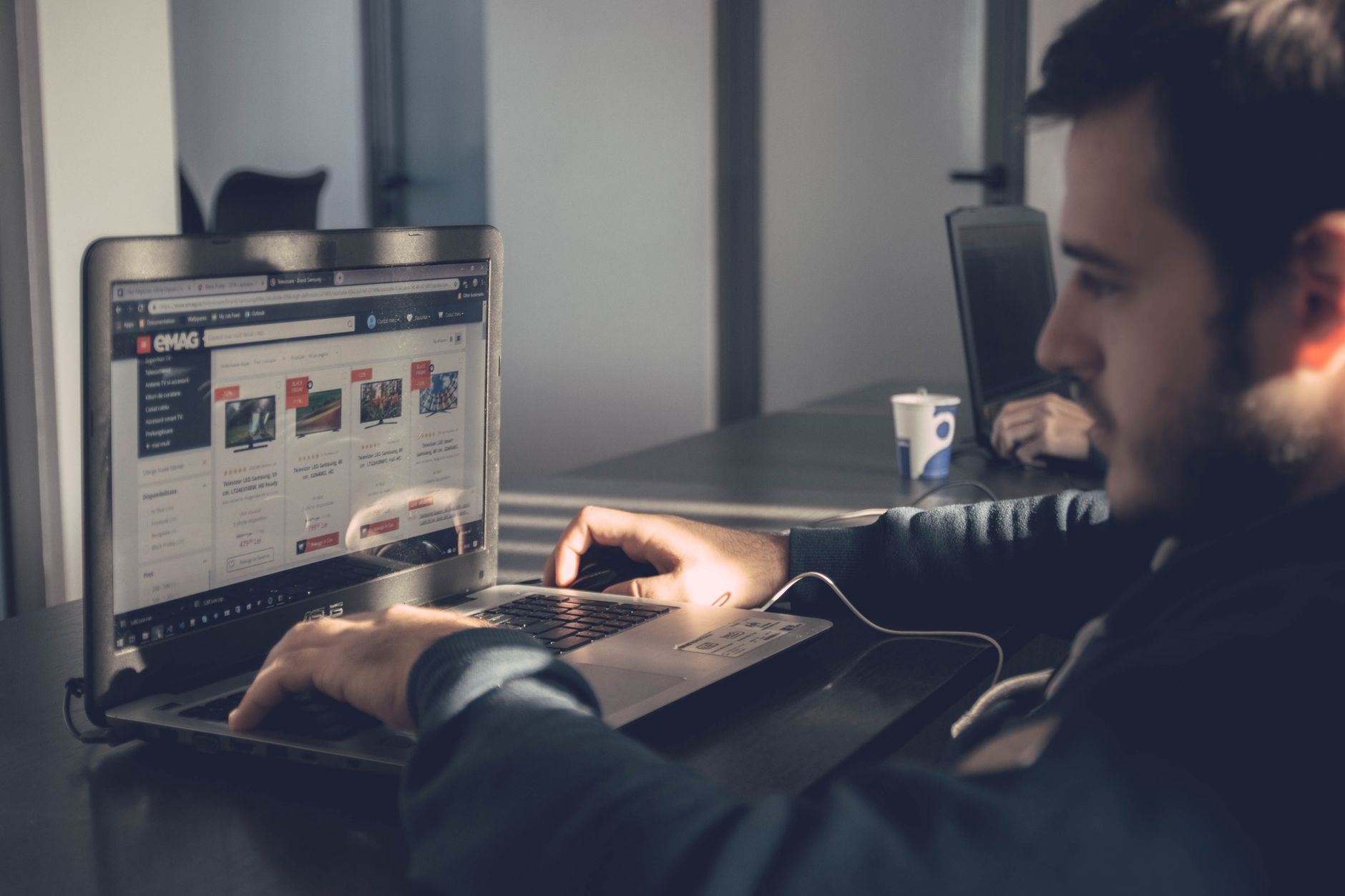 Man viewing an e-commerce website with product listings on a laptop screen
