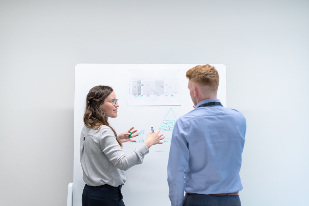 Two professionals discuss information on a whiteboard, considering e-commerce solutions