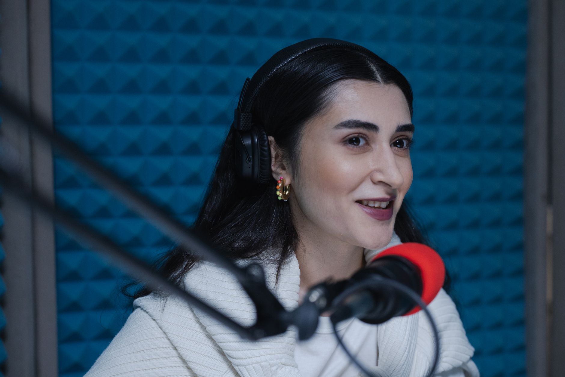 Smiling woman wearing headphones recording a podcast in a studio