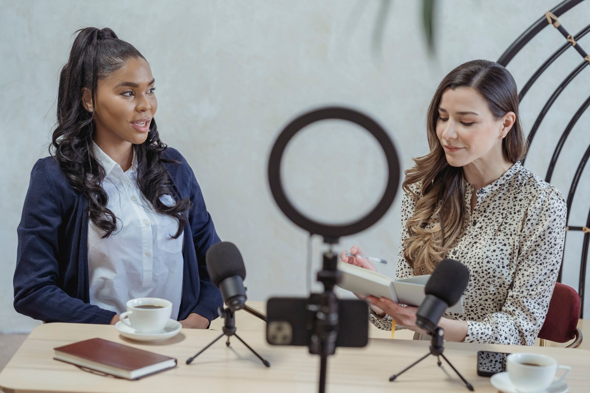 Two women with microphones, ring light, and phone, recording a podcast interview