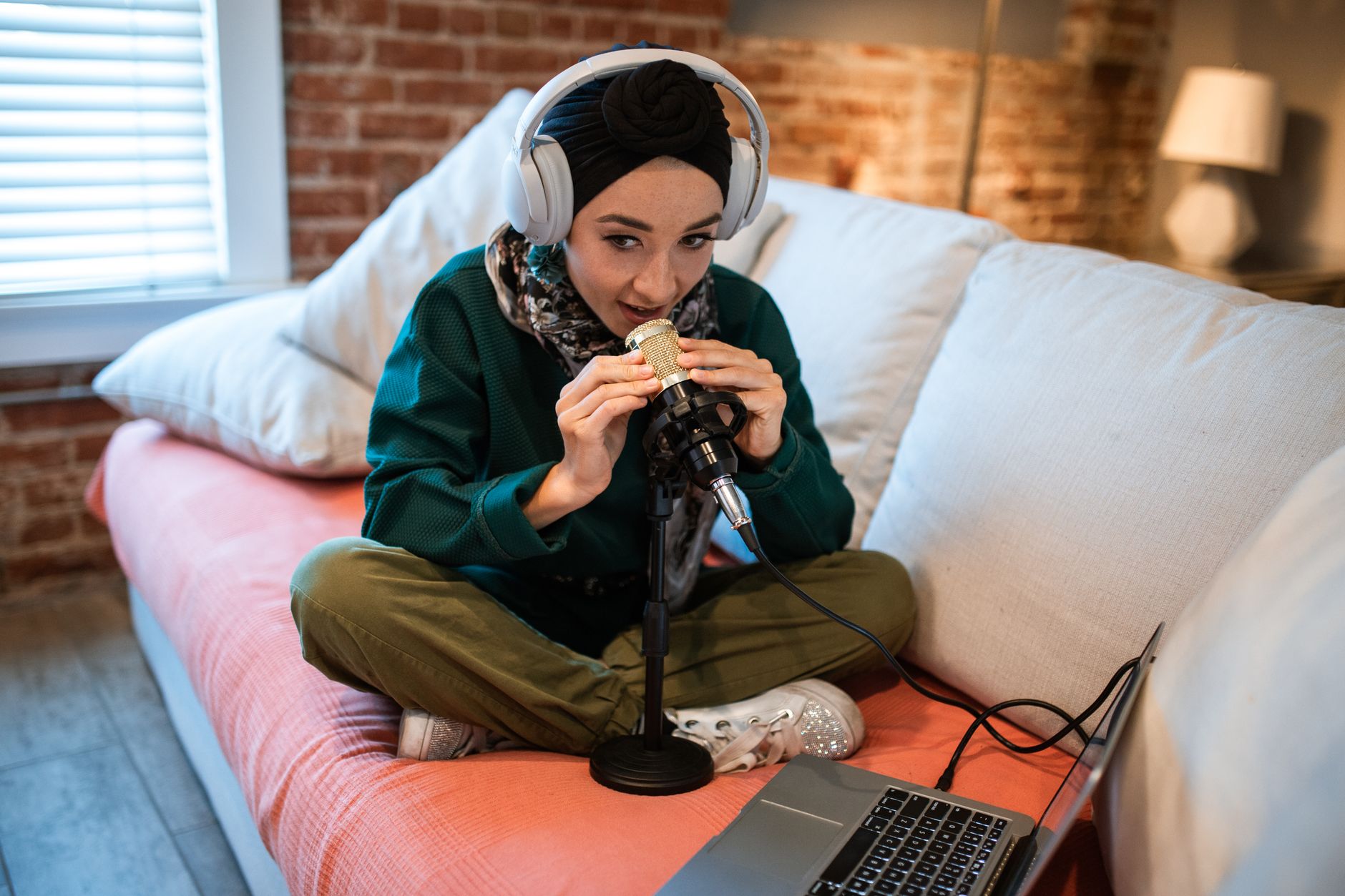 Woman in headphones records a podcast with a microphone and laptop on a couch