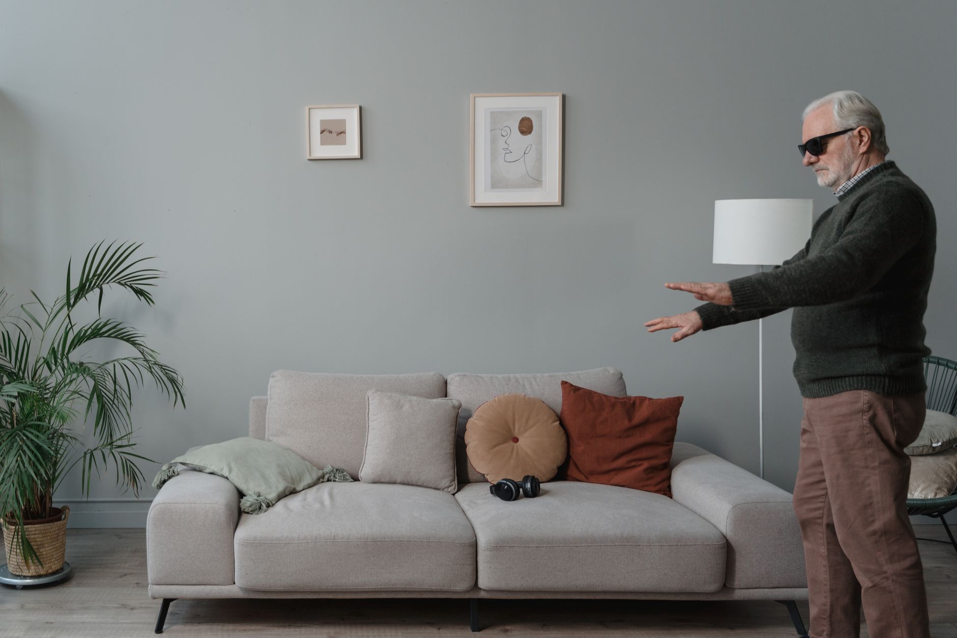Elderly man with dark sunglasses reaching out, navigating a living room alone