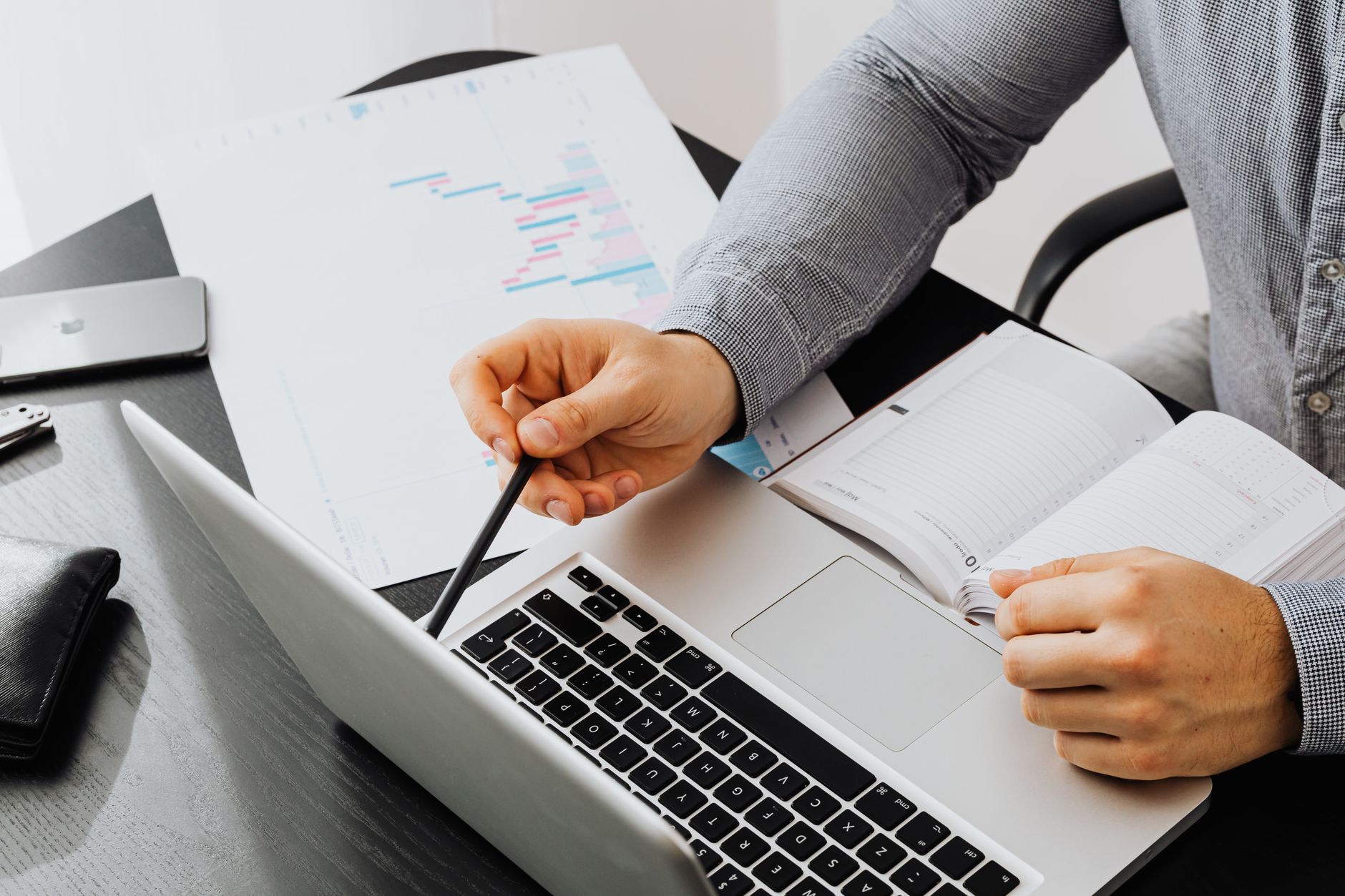A person analyzes data on a laptop and paper with a pencil and notebook