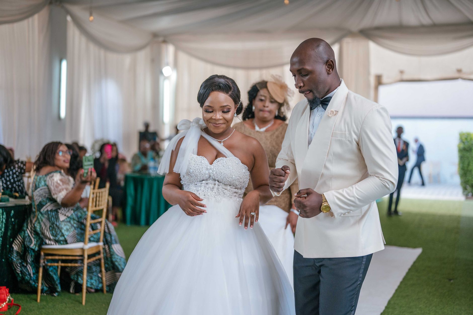 A bride and groom walk together at a wedding reception inside a draped event hall
