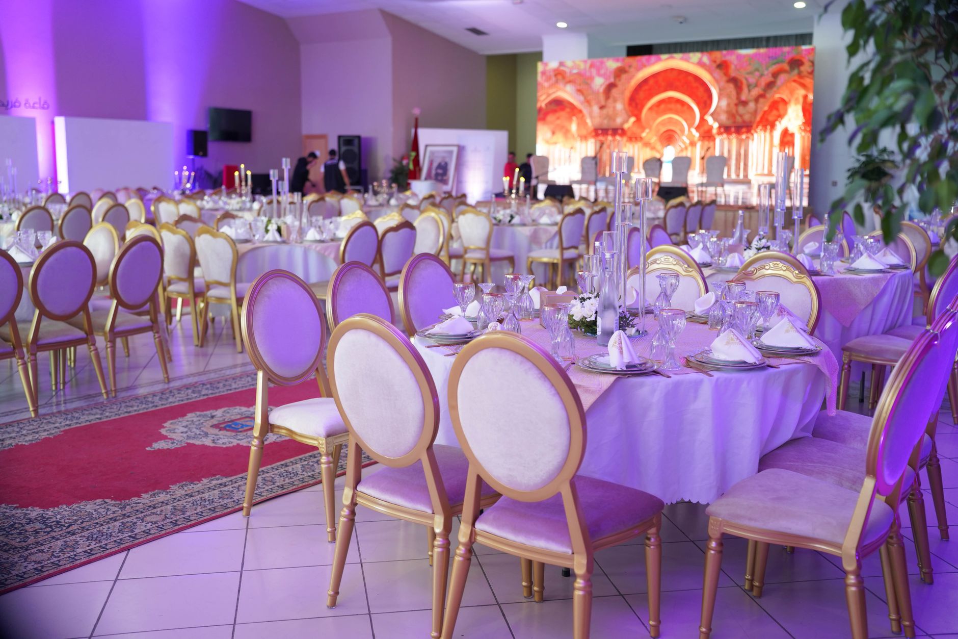 Lavishly decorated event center hall with many tables, purple lighting, and ornate chairs