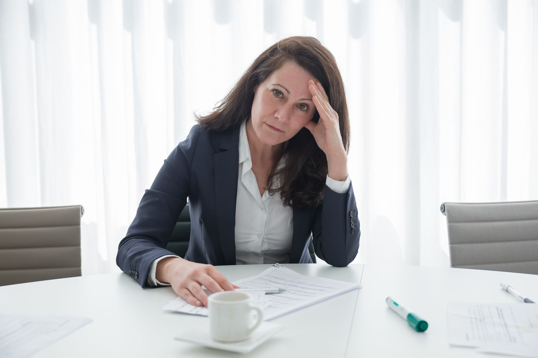 Stressed woman at a desk with papers, contemplating SEO costs and decisions