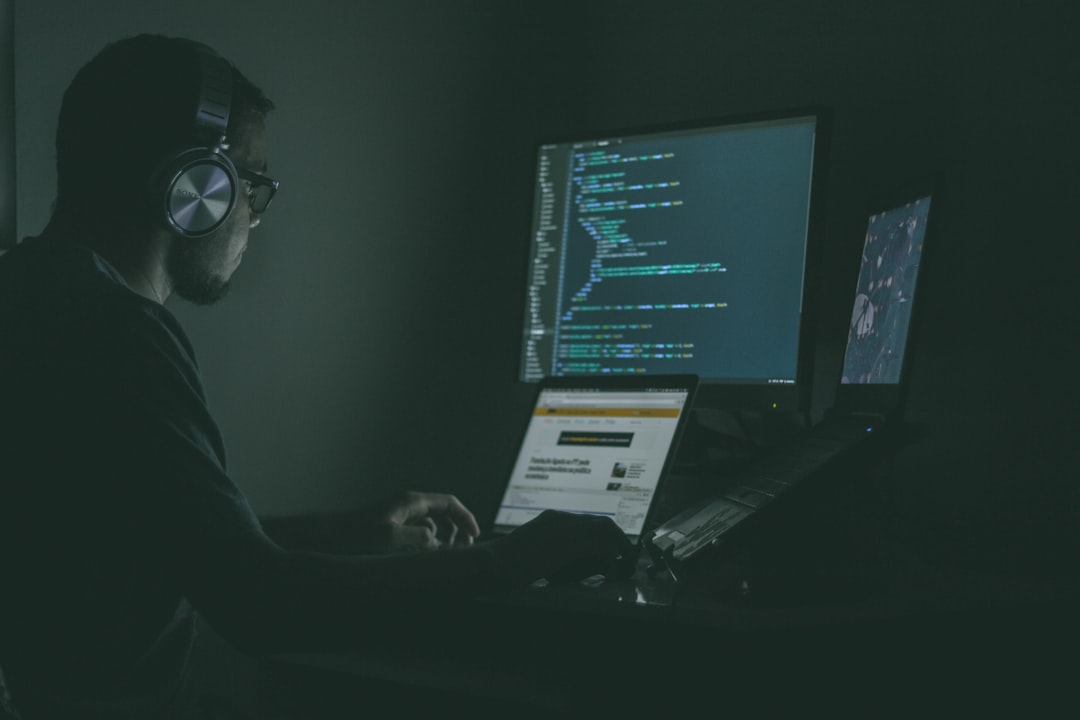 A web developer codes on multiple computer screens in a dark room