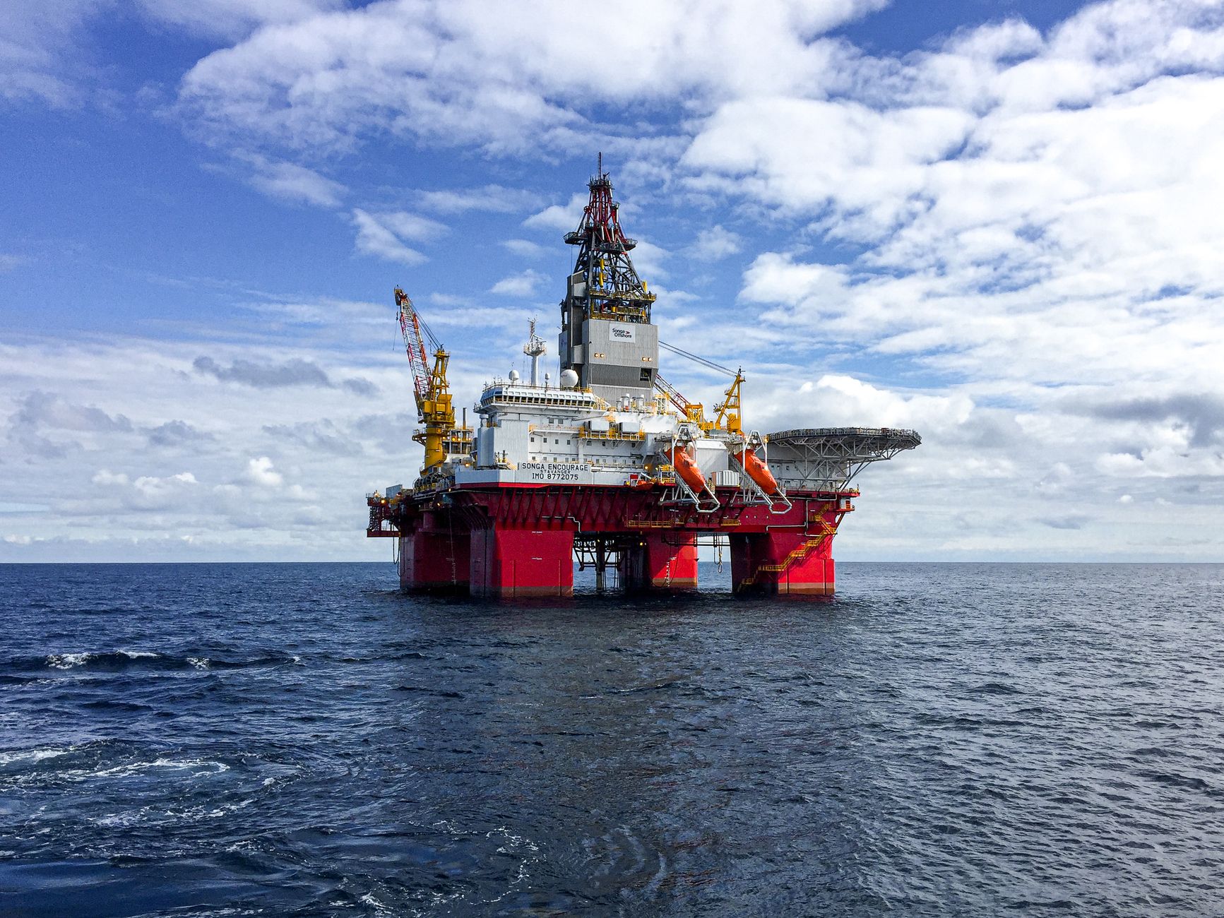 A large red and white semi-submersible offshore drilling rig in open water