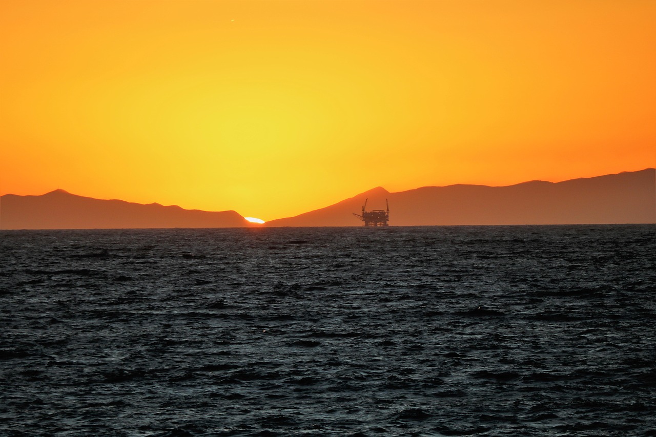 Oil rig offshore at sunset with mountains and dark ocean foreground