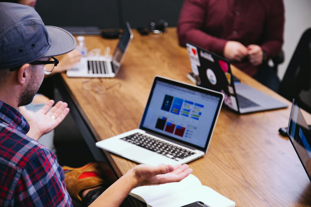 A man gestures with open hands toward a laptop on a wooden table